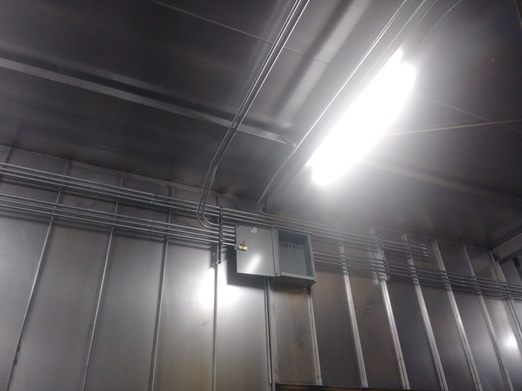 Industrial electrical conduit, panel, and lighting installation on a stainless steel wall by Bison Electrical Services in Norman, OK.