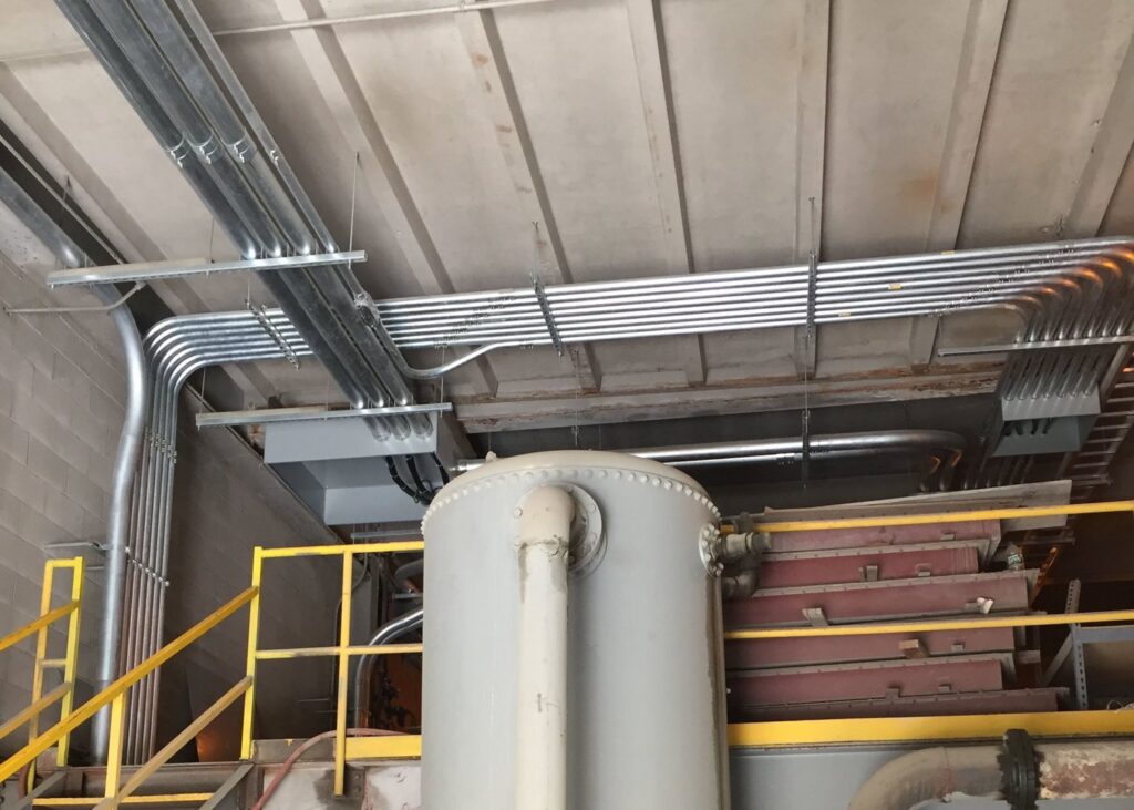 Neatly installed industrial electrical conduit runs on a ceiling and wall by Progressive Electrical Services, Inc. Lee, NH.