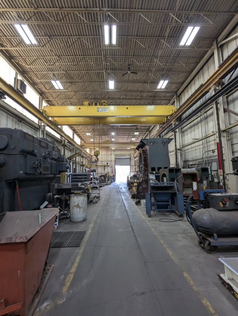 A spacious industrial electrical workshop with heavy machinery and overhead cranes, showcasing the facility of Hannon Electric Company in Canton, OH.