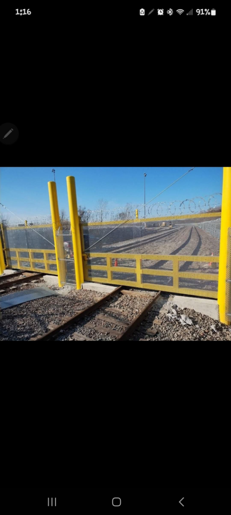 An industrial yellow fence with barbed wire and a gate installed across railroad tracks by ALL STAR FENCE in Chicago, IL.