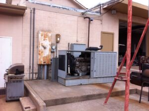 A large industrial generator and electrical panels installed on the side of a commercial building by Generator Experts of Oklahoma in Norman, OK.