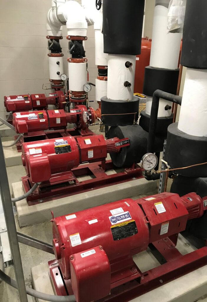 Multiple large red industrial HVAC pumps and associated piping in a mechanical room, maintained by Heinz HVAC & Plumbing in Vincennes, IN.