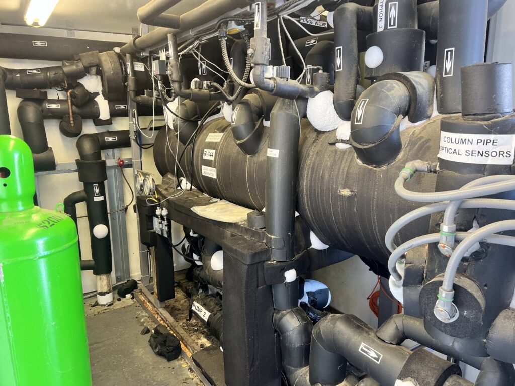 A complex industrial refrigeration or HVAC system with insulated pipes, serviced by Advanced Comfort LLC in Concord, NH.