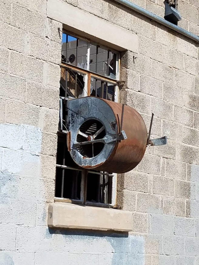 An industrial ventilation fan unit installed in a building window, representing work by Avallone Mechanical Company in Las Cruces, NM.