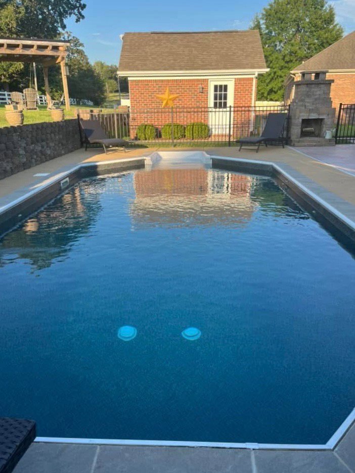 An inground pool with a dark liner and extensive concrete decking, showcasing a completed project by Riverstone LLC in Bowling Green, KY.