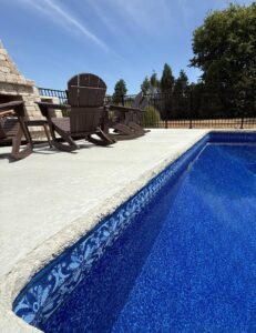 A long inground pool with concrete decking, lounge chairs, and an integrated stone fire pit, built by Riverstone LLC in Bowling Green, KY.