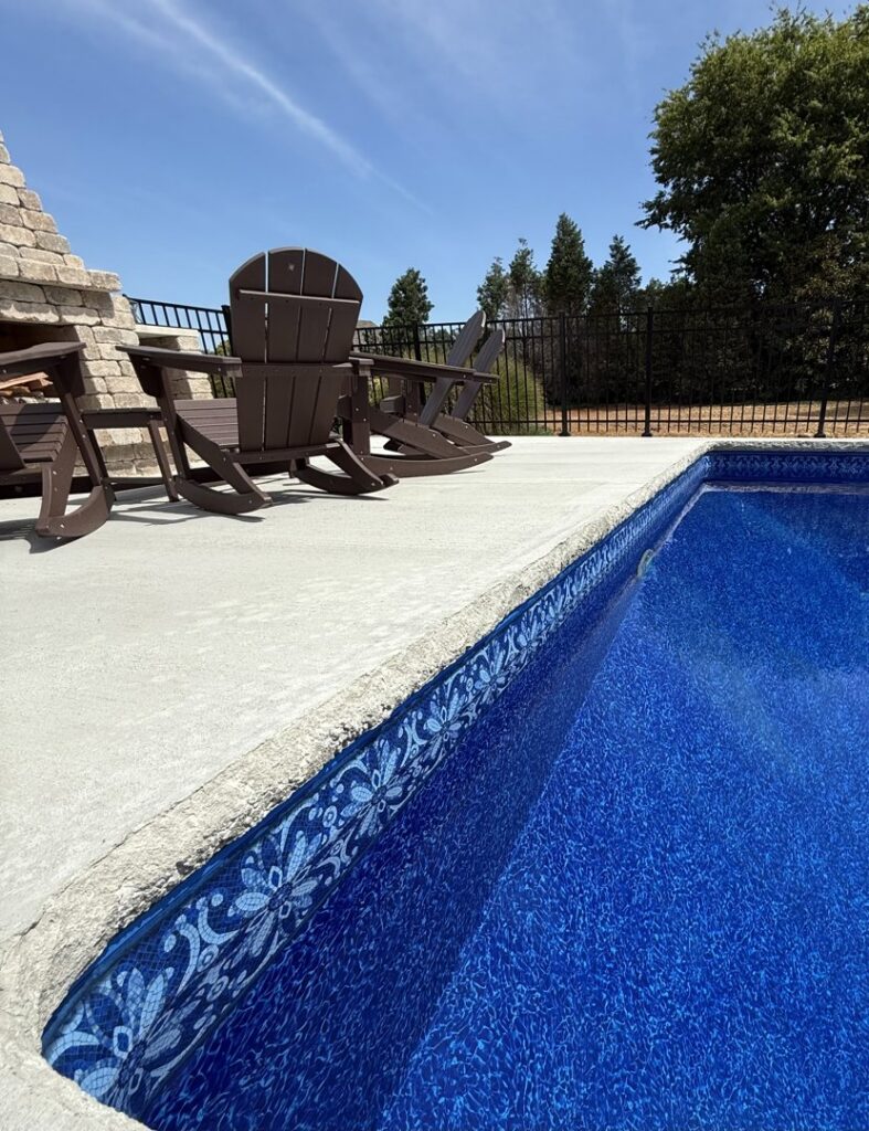 A long inground pool with concrete decking, lounge chairs, and an integrated stone fire pit, built by Riverstone LLC in Bowling Green, KY.