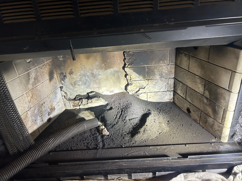 A vacuum hose removing heavy soot and creosote buildup from inside a fireplace by The Chimney Guys in Jackson, TN.