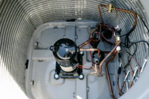 An internal view of an outdoor AC unit, showcasing the compressor and copper refrigerant lines, by Wingman Heating + Cooling in Auburn, AL.