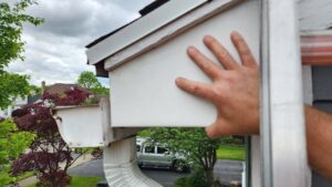 A hand inspecting damaged soffit on a house, identifying potential wildlife entry points for Armstrong's Wildlife Solutions in Rochester, NY.
