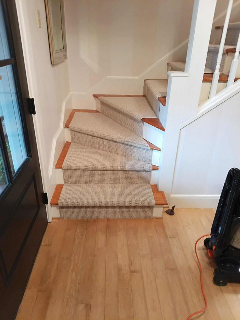 A beautifully installed light-colored carpet runner on a wooden staircase by Onondaga Flooring in Syracuse, NY.