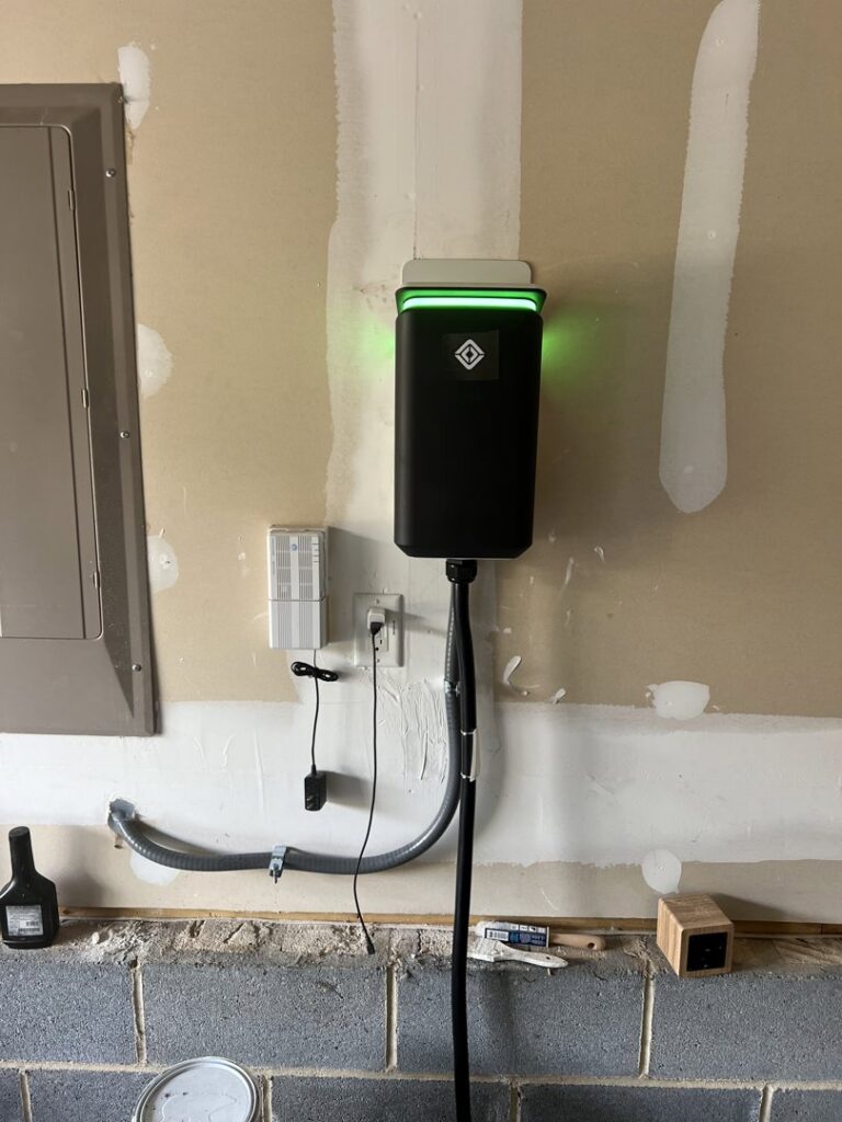 A newly installed EV charger on a garage wall with visible conduit and wiring by Green Volt Electric LLC in Durham, NC.