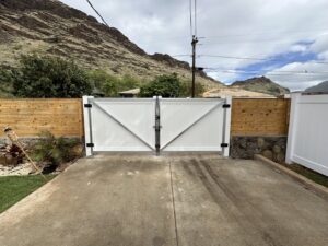A newly installed white double gate with wooden privacy fences on either side by Upright Fencing Hawaii LLC in Kapolei, HI.