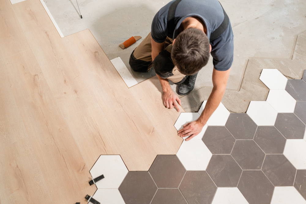 An installer laying hexagonal tile and wood-look planks, showcasing flooring services by Carpet One Topeka in Topeka, KS
