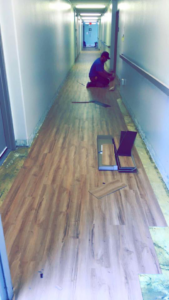 An installer laying laminate flooring in a hallway, demonstrating a service by Capitol Carpet Co in Sherman Oaks, CA