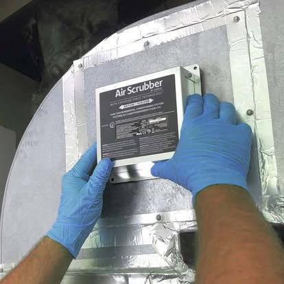 Hands in blue gloves installing an Air Scrubber device into ductwork for Fields Cooling Heating & Refrigeration in Foley, AL.