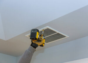 A hand installing a ceiling air vent with a drill for Greater Boston Heating & Air in Boston, MA.
