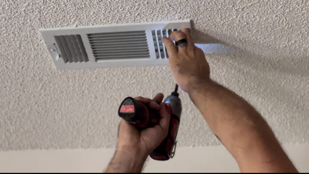 Hands using a drill to install or remove a ceiling air vent as part of HVAC service by Anderson Mechanical Inc. in Pascagoula, MS