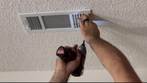 Hands using a drill to install or remove a ceiling air vent as part of HVAC service by Anderson Mechanical Inc. in Pascagoula, MS