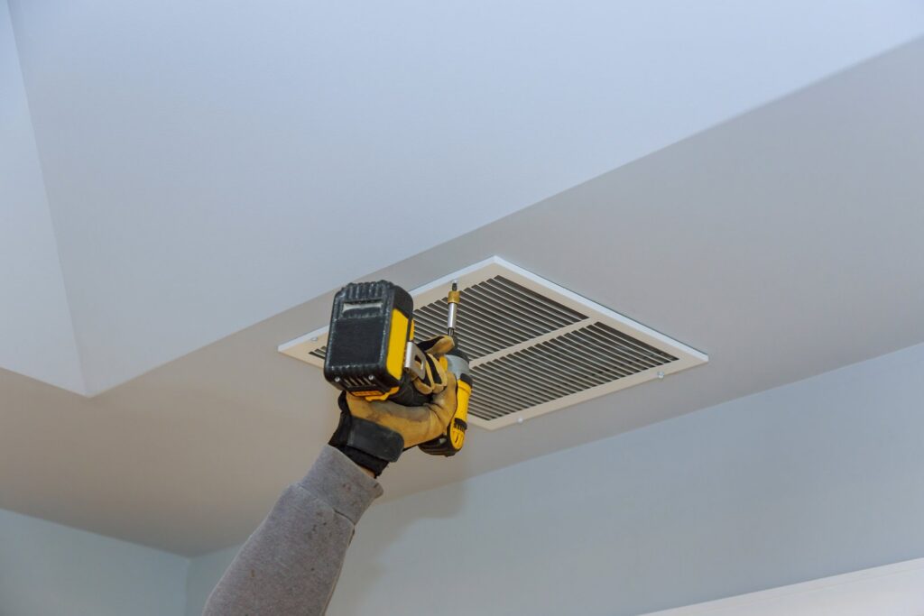 A gloved hand using a power drill to install a ceiling air vent, part of HVAC service by Jons-Air in Carmel, IN.