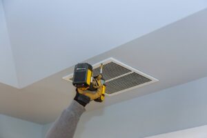 A gloved hand using a power drill to install a ceiling air vent, part of HVAC service by Jons-Air in Carmel, IN.