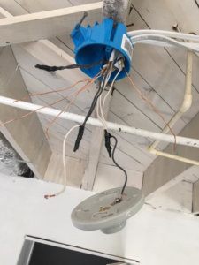 An electrician installing a ceiling light fixture with exposed wiring for U-R Wired in Baltimore, MD.