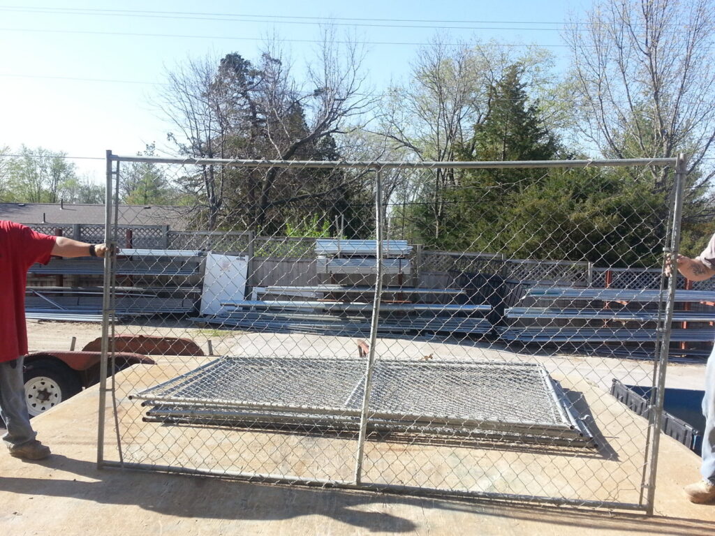 Two workers installing a chain-link fence panel for James Fencing LLC in Columbia, MO.