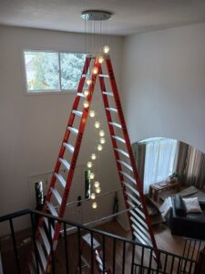 An electrician installing a large, multi-tier chandelier using a tall ladder for Midway Electric Inc. in Columbia, MO.