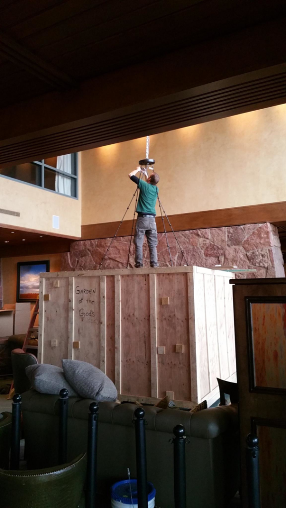 An electrician installing a large chandelier into a ceiling, a service provided by Rockhill Electrical Systems in Colorado Springs, CO.