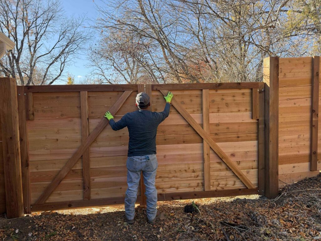 A fencing contractor installing a large wood privacy gate for a client in Denver, CO, by Supreme Fencing.