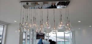 Electricians On Call installing a large, modern chandelier in Fort Lauderdale, FL.