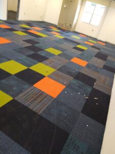 A professional installing multi-colored carpet tiles for Jungle Jim's Floorcovering in Anchorage, AK.