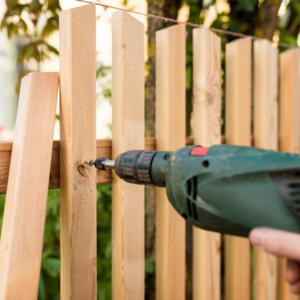 A person installing a wooden fence picket with a drill, showcasing work by David's Fencing Inc. in Waipahu, HI.