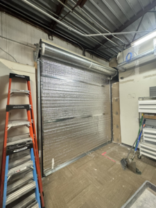 Interior view of an insulated commercial roll-up garage door with a ladder, installed by Roll-Rite Garage Doors in Denver, CO.
