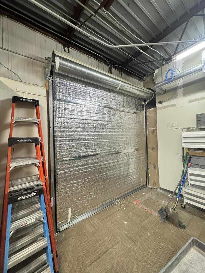 Interior view of an insulated commercial roll-up garage door with a ladder, installed by Roll-Rite Garage Doors in Denver, CO.