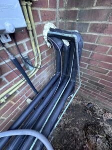 Insulated HVAC refrigerant lines running along the exterior brick wall of a building by Oakes AC Services, LLC in Louisburg, NC