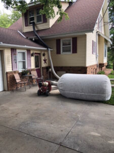 A large hose and bag connected to a house window, indicating insulation removal or installation as part of critter remediation by Aksarben Bat & Critter Removal in Omaha, NE