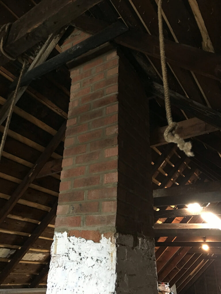 An interior view of a brick chimney stack in an attic, showing its structure, relevant for inspection by Chimney Usa Inc in Chicago, IL.