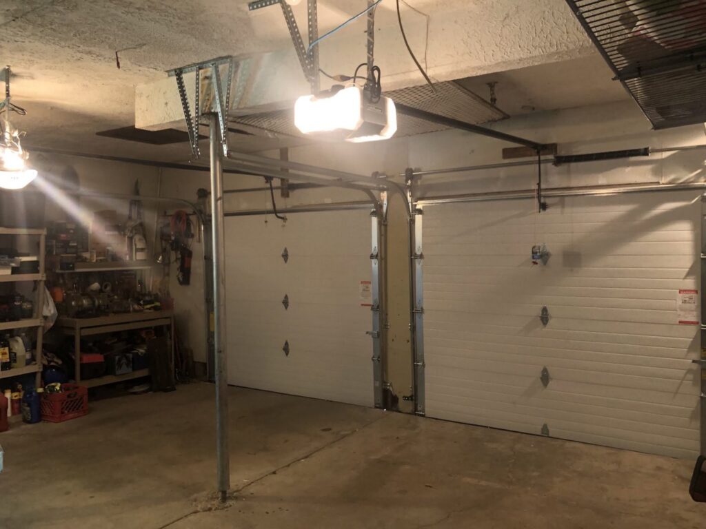 The interior of a garage showing two white garage doors with their tracks and openers, installed by Garage Doors Of Indianapolis in Indianapolis, IN