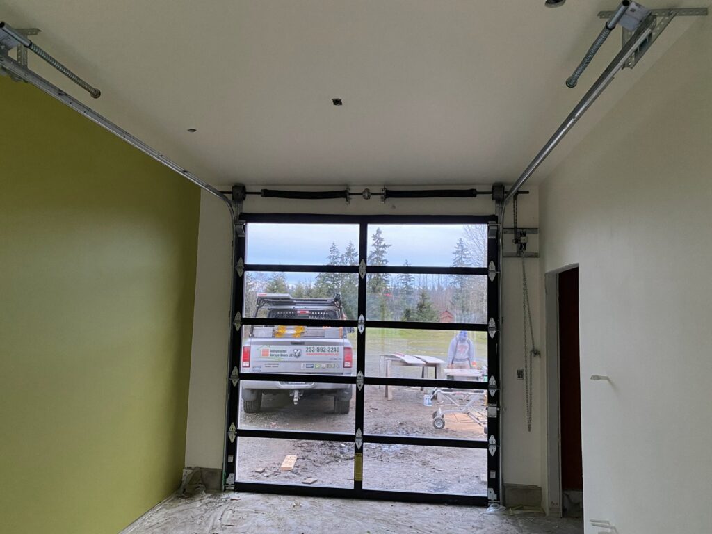 Interior view of a garage showing a modern glass garage door with tracks and opener mechanism installed by Independent Garage Doors LLC in Tacoma, WA.
