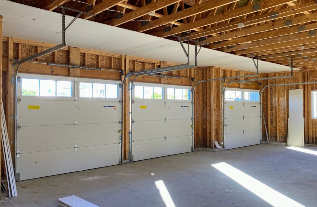 Interior view of a three-car garage with newly installed white garage doors and tracks by Superior Overhead Door, LLC in Granger, IN