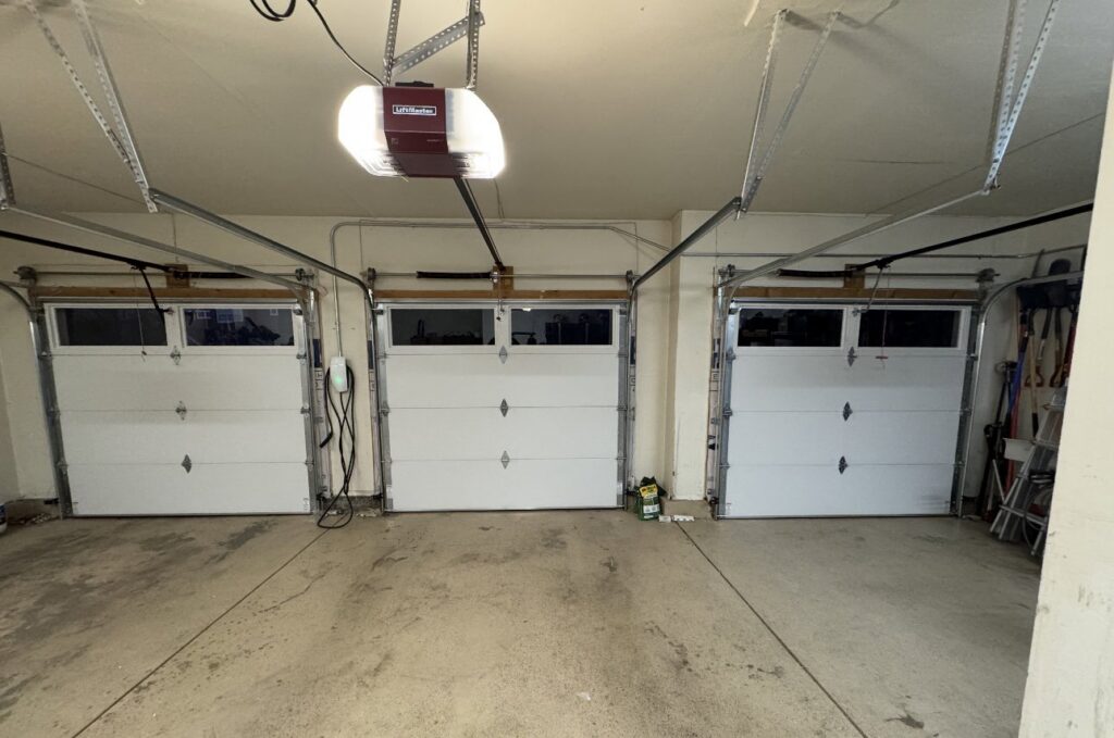 Interior view of three newly installed white garage doors and openers by Lion Heart Garage Doors in Thornton, CO.