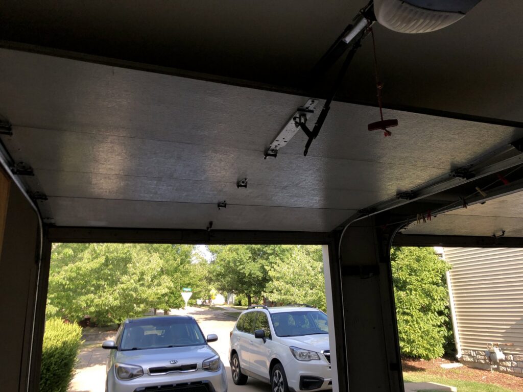 An interior view of an open garage door, showing the mechanism and cars in the driveway, serviced by Overhead Door Company of Central Missouri in Columbia, MO.