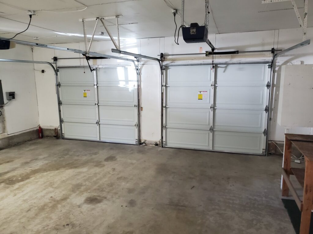 Interior view of two newly installed white garage doors with openers by Steadfast Garage Door Services LLC in Federal Way, WA.