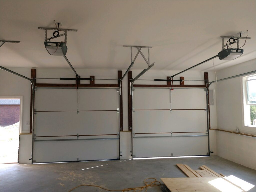 Interior view of a garage showing two white garage doors and openers fully installed by Ken's Overhead Door in Clarksville, TN.