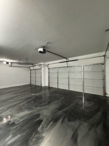 An interior view of a garage showcasing two newly installed white garage doors and openers by JT's Overhead Doors in Gilbert, AZ.