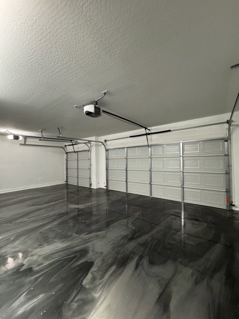 An interior view of a garage showcasing two newly installed white garage doors and openers by JT's Overhead Doors in Gilbert, AZ.