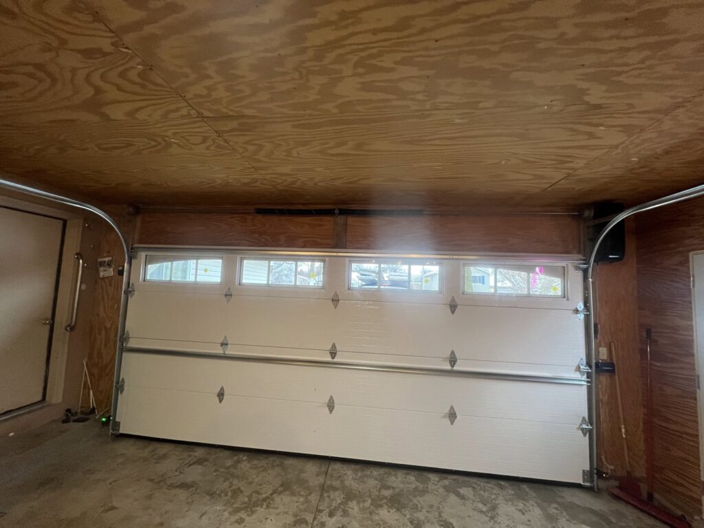An interior view of a garage showing a newly installed white garage door with windows by McDonald Overhead Door Inc. in Kenosha, WI.