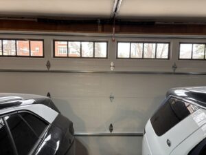 An interior view of a white garage door with windows, partially open, with two cars inside by AJK Door Services in Duluth, MN.