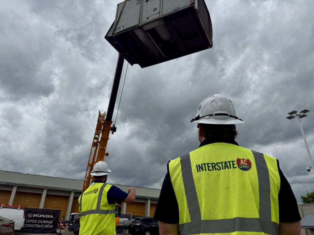 Interstate AC technicians observing a crane lifting a large HVAC unit at a job site in Nashville, TN.